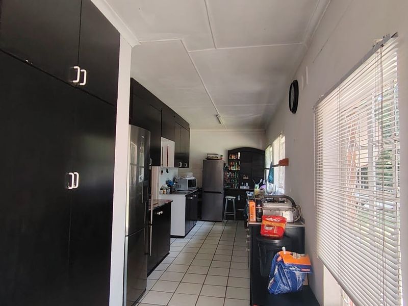 A functional kitchen featuring dark built-in cabinetry, tiled flooring, and natural light provided by large windows with fitted venetian blinds.