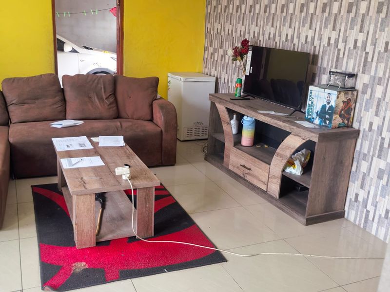 A living room featuring tiled flooring and decorative ceiling cornicing, currently requiring cosmetic updates to the wall finishes.