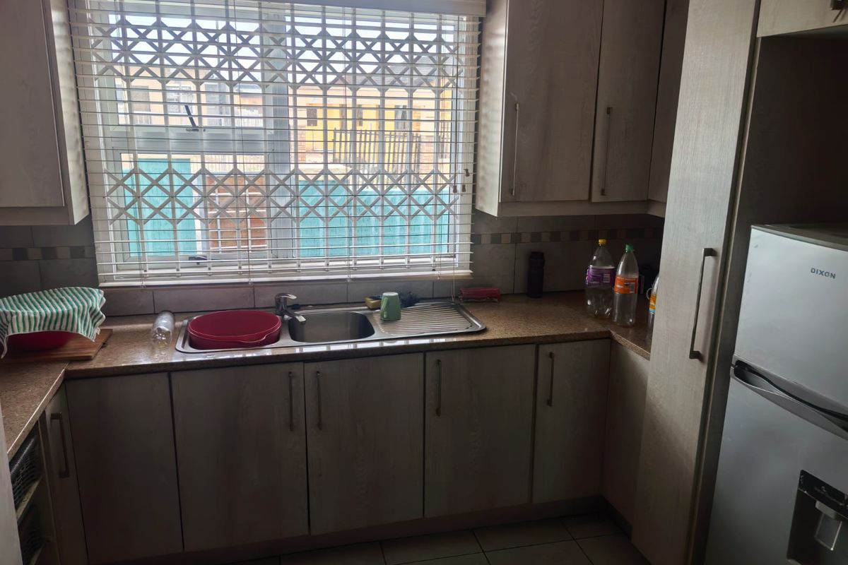 A functional kitchen featuring laminate cabinetry, granite countertops, a stainless steel sink, and tiled flooring, with a security gate installed on the window.