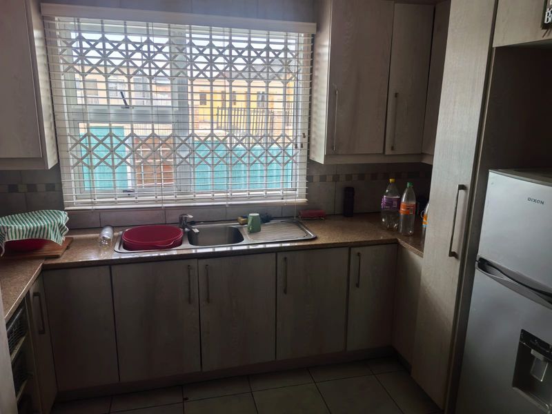 A functional kitchen featuring laminate cabinetry, granite countertops, a stainless steel sink, and tiled flooring, with a security gate installed on the window.