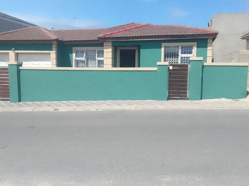 Front elevation of a single-story house featuring a tiled roof, secure boundary wall with pedestrian and vehicle access, and security bars on windows.