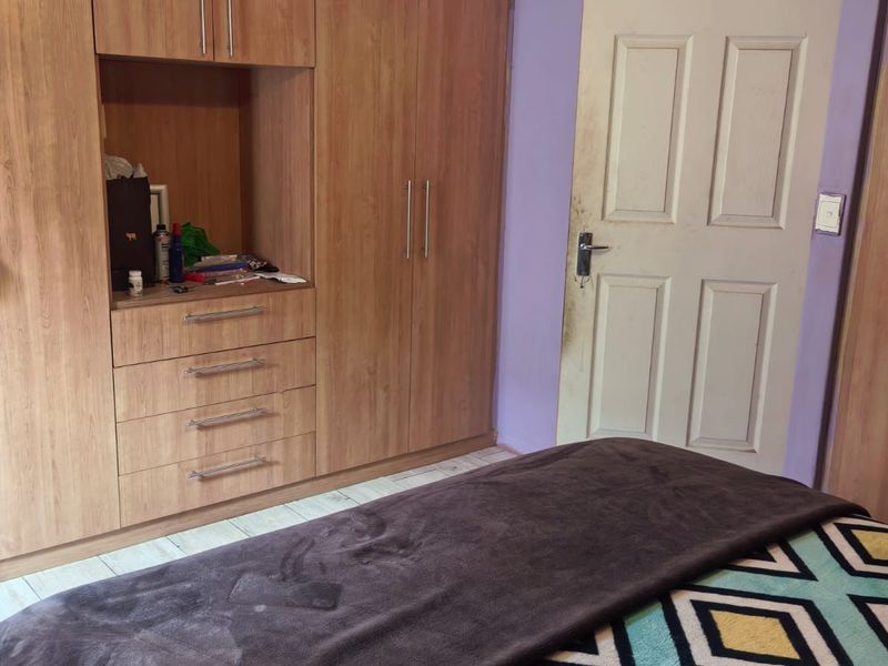 Bedroom featuring built-in wooden cupboards and a standard panel door, requiring cosmetic updates to the wall finishes and ceiling trim.