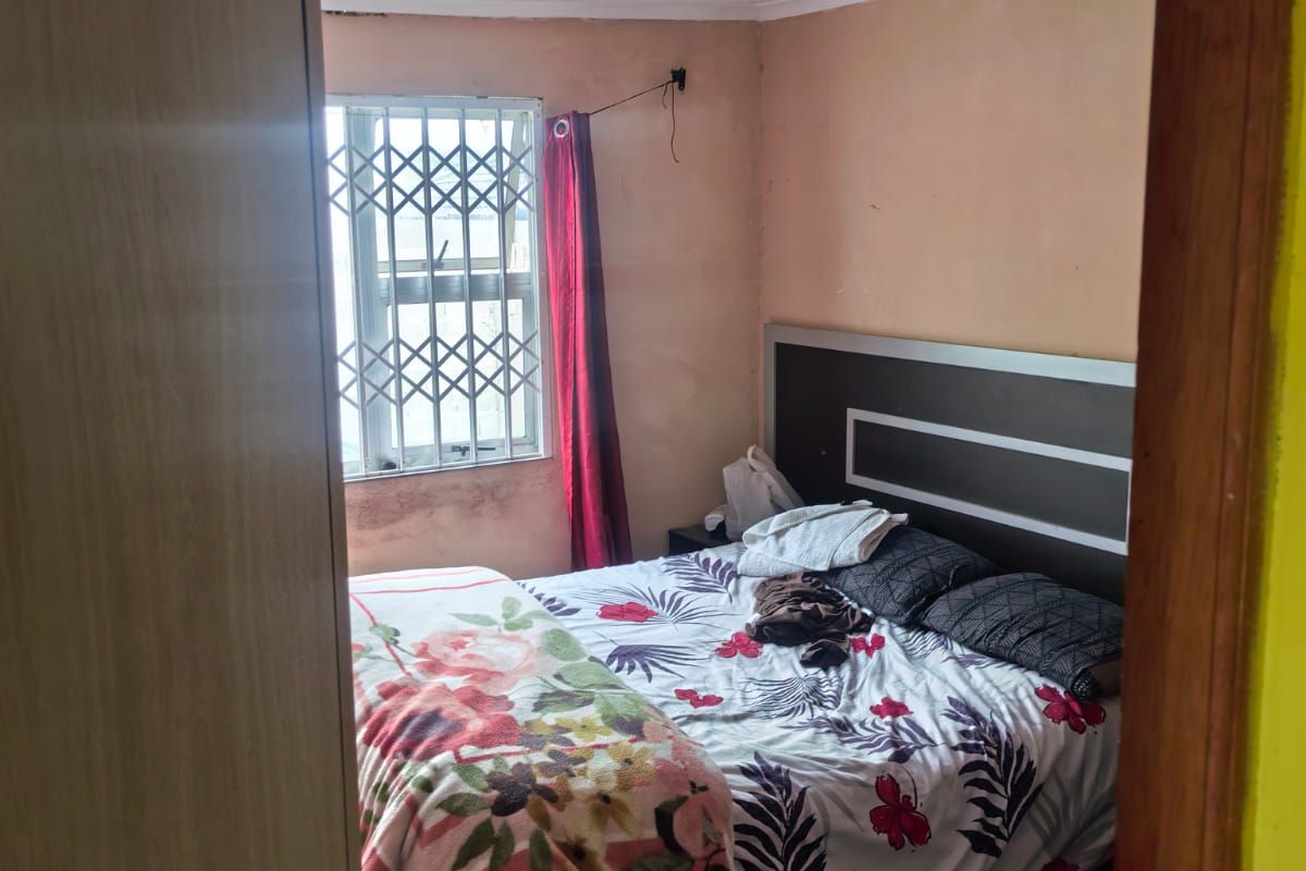 A bedroom featuring tiled flooring, a built-in headboard, and a window with a security gate. The room requires cosmetic updates to the walls.