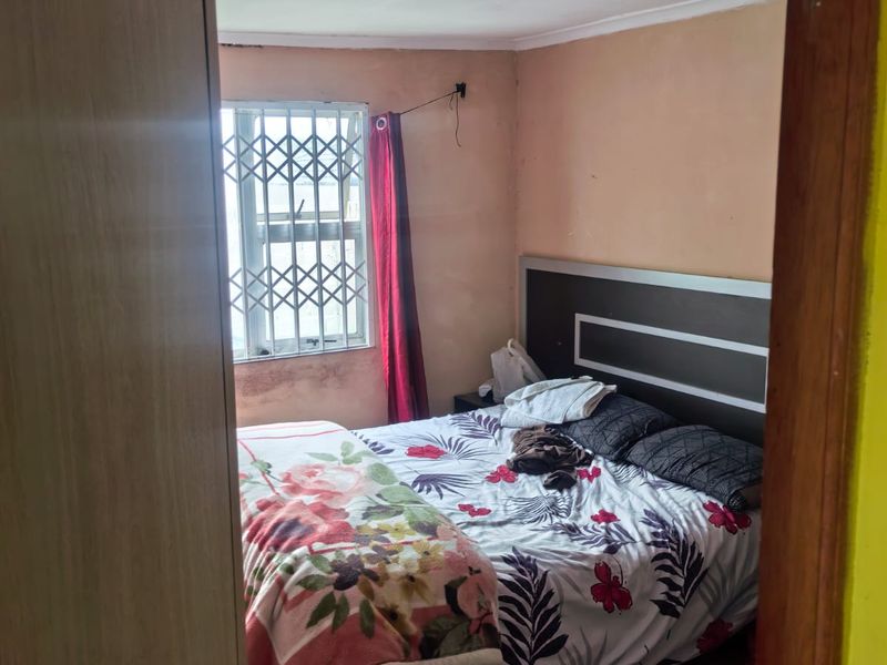 A bedroom featuring tiled flooring, a built-in headboard, and a window with a security gate. The room requires cosmetic updates to the walls.