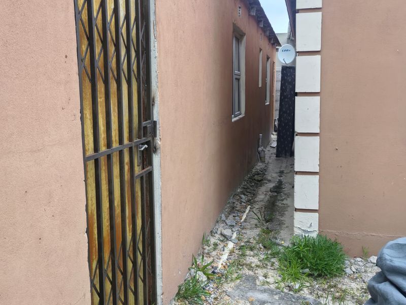 A narrow side passage between two structures featuring a security gate, concrete pathway, and exterior wall finishes requiring maintenance.