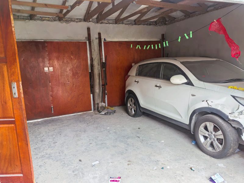 A functional garage space featuring wooden doors, exposed timber roof trusses, and concrete flooring, offering potential for storage or workshop conversion.