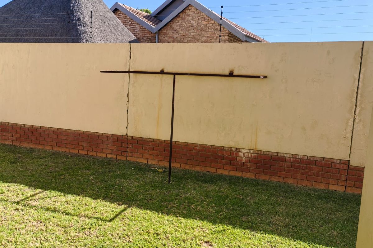 Rear garden area featuring a perimeter wall with brick base, electric fencing, and a fixed metal washing line.