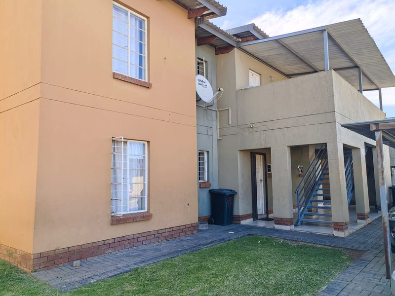 Rear view of a multi-story townhouse featuring a covered patio, external metal staircase, and brick-paved garden area.