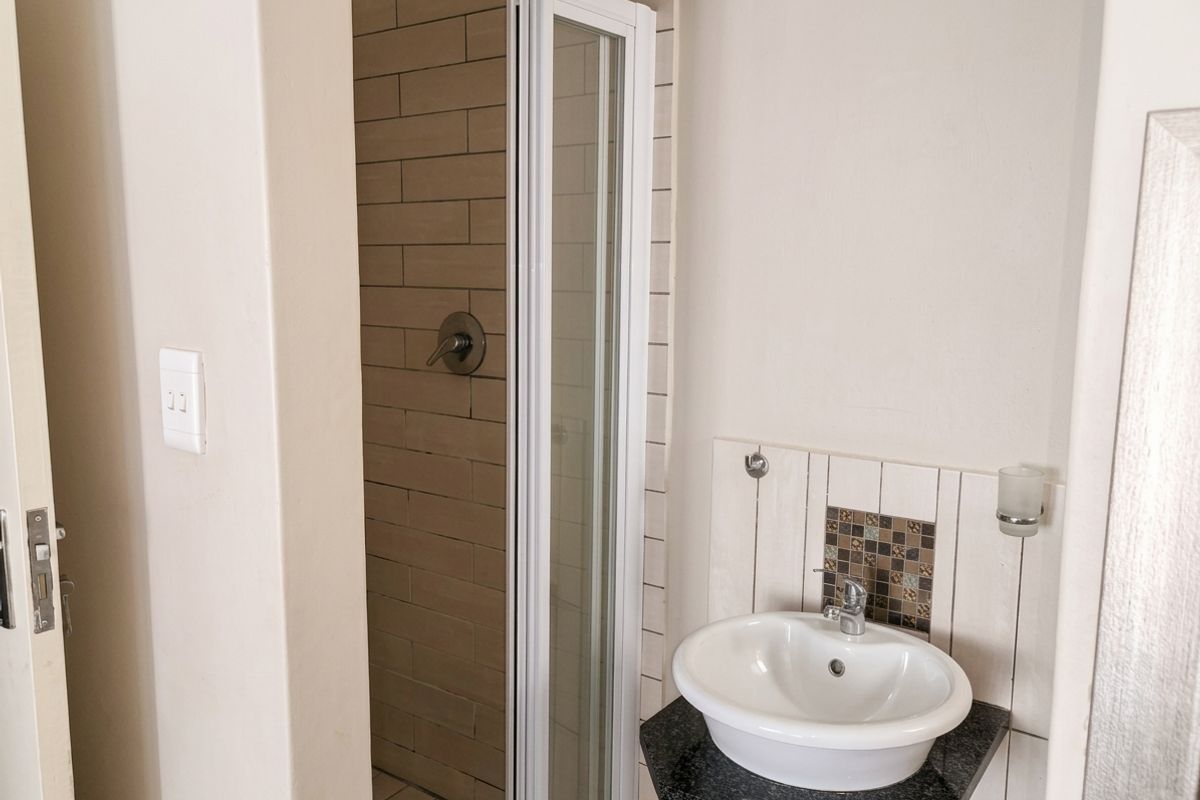A compact bathroom featuring a shower enclosure with tiled walls and a wall-mounted basin with a granite vanity top.