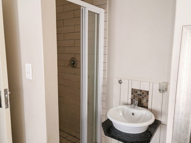 A compact bathroom featuring a shower enclosure with tiled walls and a wall-mounted basin with a granite vanity top.