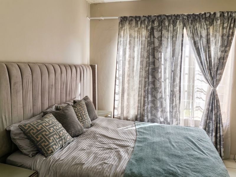 A bedroom featuring a window with a curtain rod, showing signs of wear on the ceiling and wall finishes.