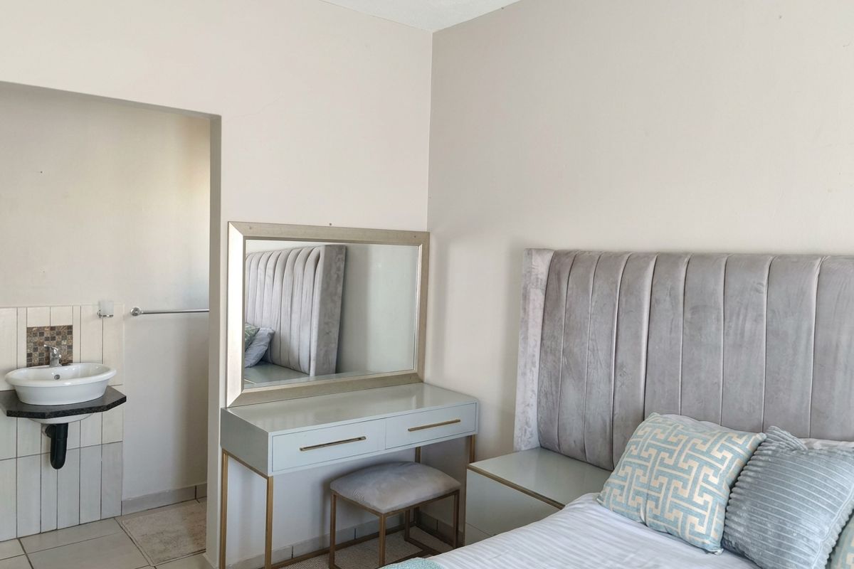 A bedroom featuring a neutral color palette with an integrated vanity area and an adjacent open-plan basin setup.