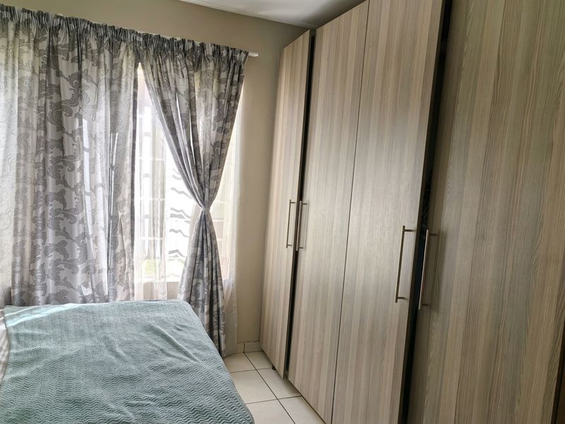 A bedroom featuring light wood-grain built-in wardrobes and tiled flooring, providing ample storage space and a neutral aesthetic.
