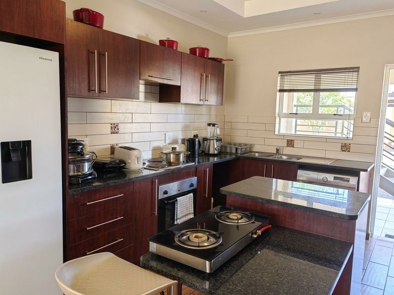 A functional kitchen featuring dark wood cabinetry, granite countertops, a built-in oven, gas hob, and a subway tile backsplash with natural light.