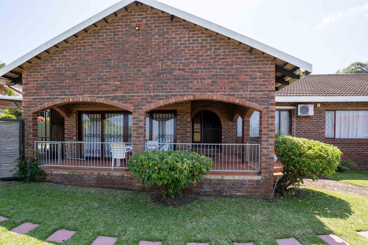 A rear view of the house featuring a covered patio with arched brick detailing, metal security gates, and a well-maintained garden area.