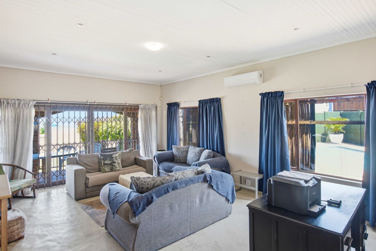 Spacious living room featuring tiled flooring, timber ceiling, and security gates leading to the outdoor area, equipped with a wall-mounted air conditioning unit.