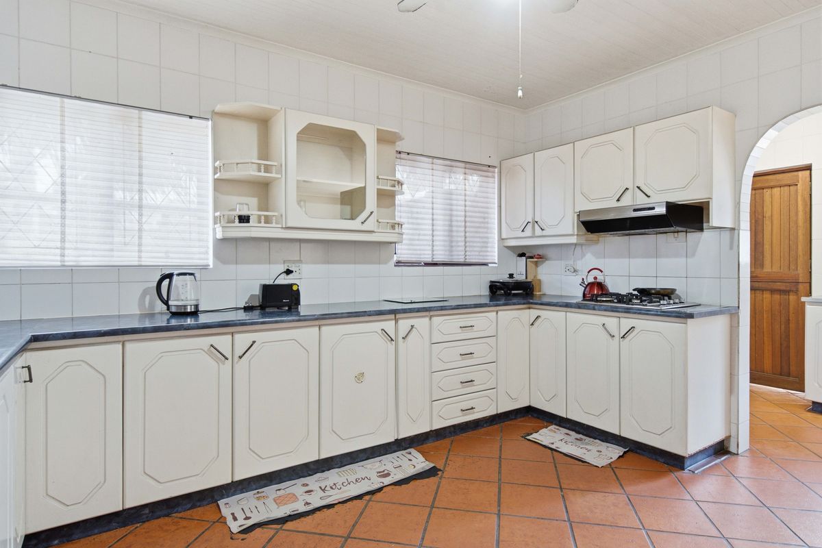 A functional kitchen featuring white built-in cabinetry, dark laminate countertops, a gas hob with extractor fan, and traditional terracotta floor tiles.