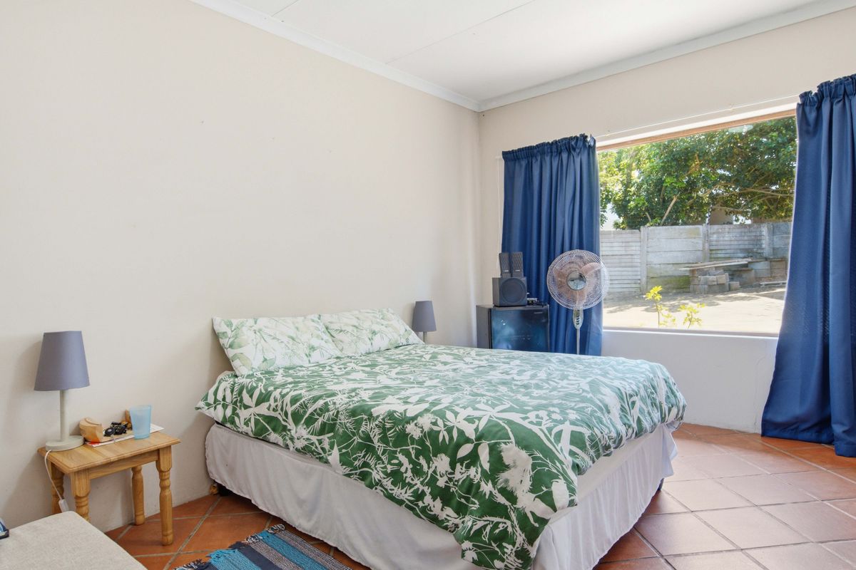 A functional bedroom featuring tiled flooring and a large window providing natural light and garden views.