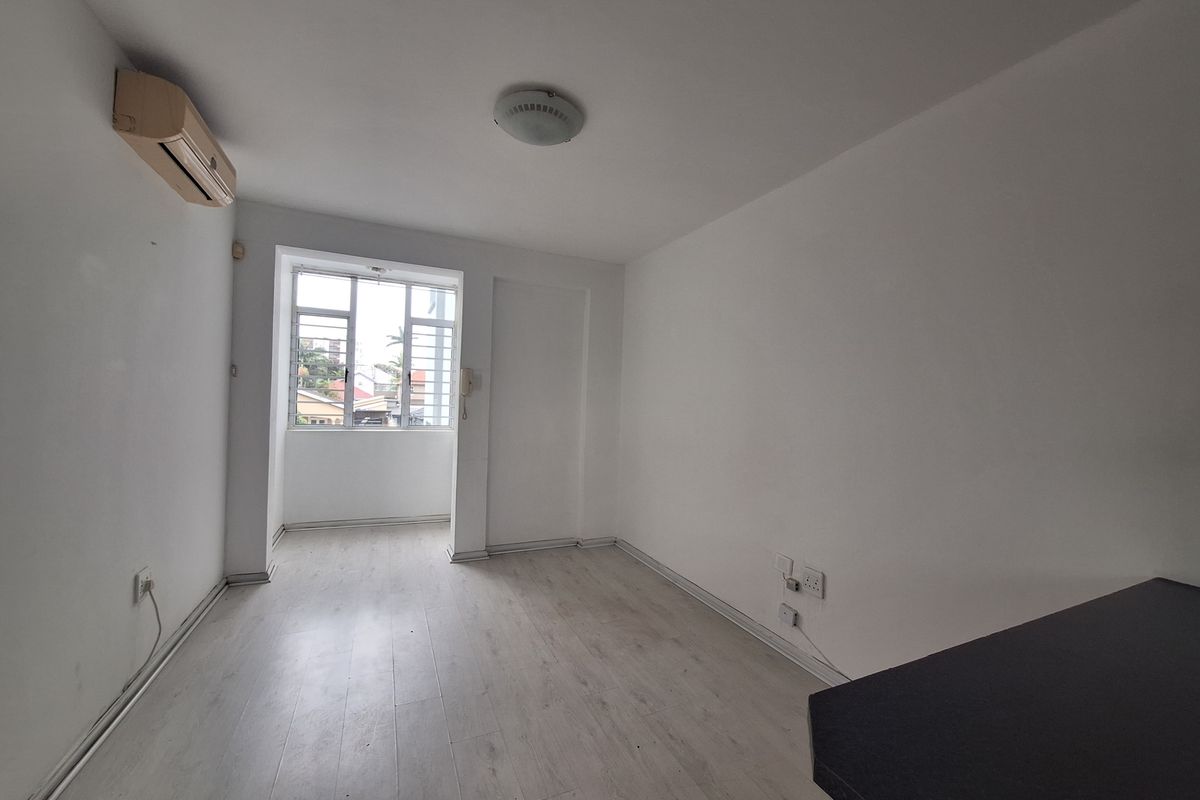 An empty bedroom featuring light-toned laminate flooring, a wall-mounted air conditioning unit, and a window with security bars.