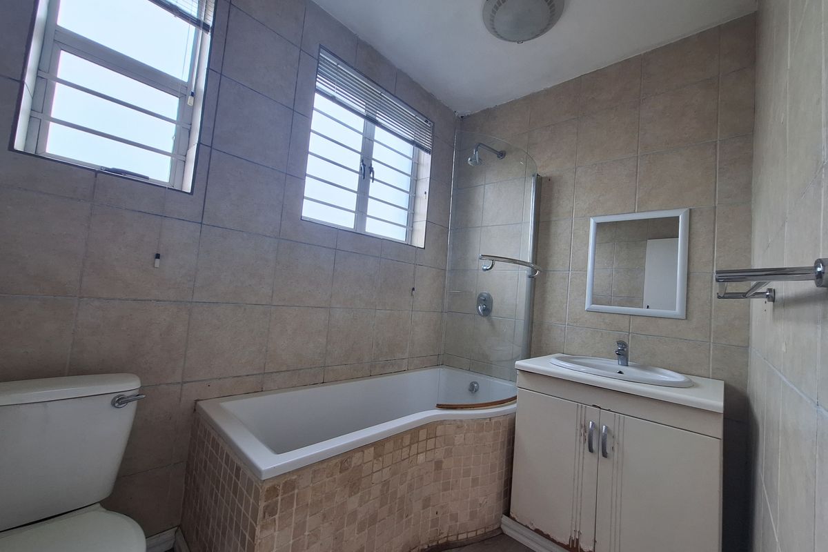 A functional bathroom featuring a bathtub with shower screen, vanity basin, and toilet, finished with neutral wall tiling.