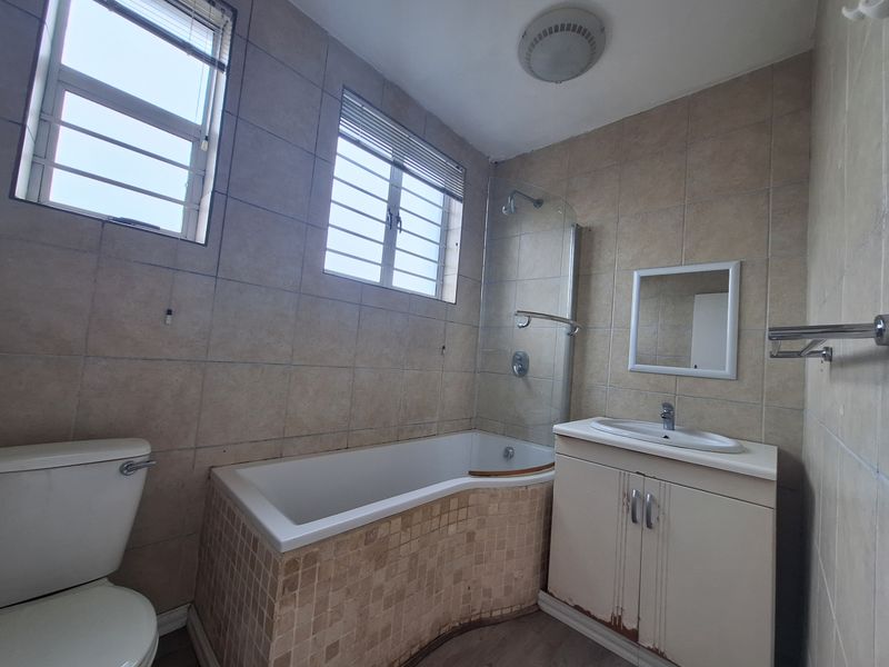 A functional bathroom featuring a bathtub with shower screen, vanity basin, and toilet, finished with neutral wall tiling.