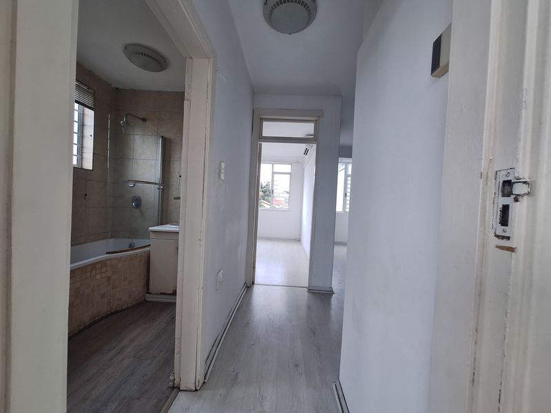 A functional hallway connecting the living area and bathroom, featuring light-toned laminate flooring and neutral wall finishes throughout the apartment.
