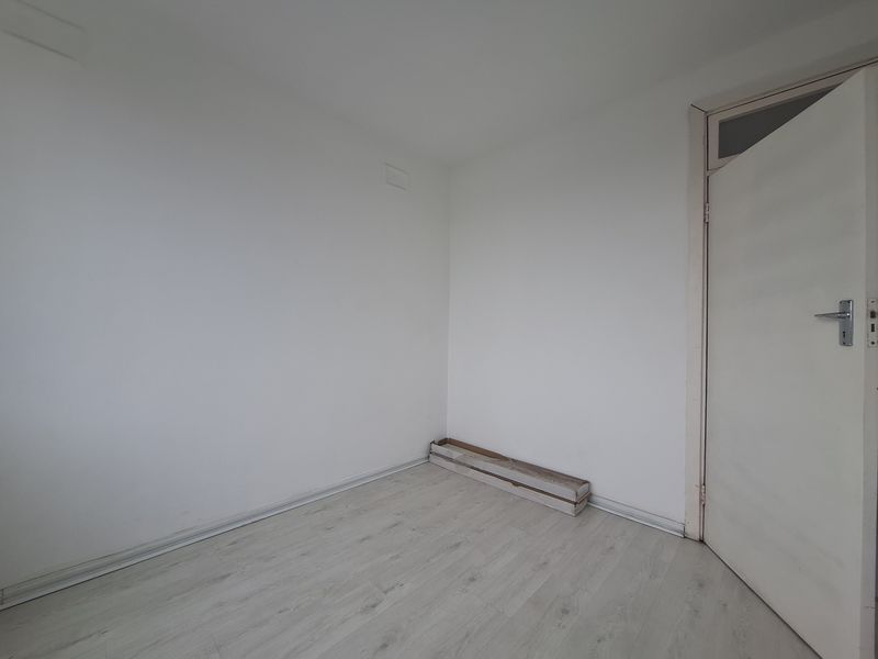 A bright, empty bedroom featuring light-toned laminate flooring and white walls, providing a clean and neutral canvas for personalization.