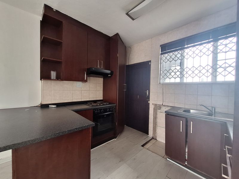 A functional kitchen featuring dark wood cabinetry, laminate countertops, built-in oven, and hob, requiring some maintenance and repairs to the flooring and cabinetry.
