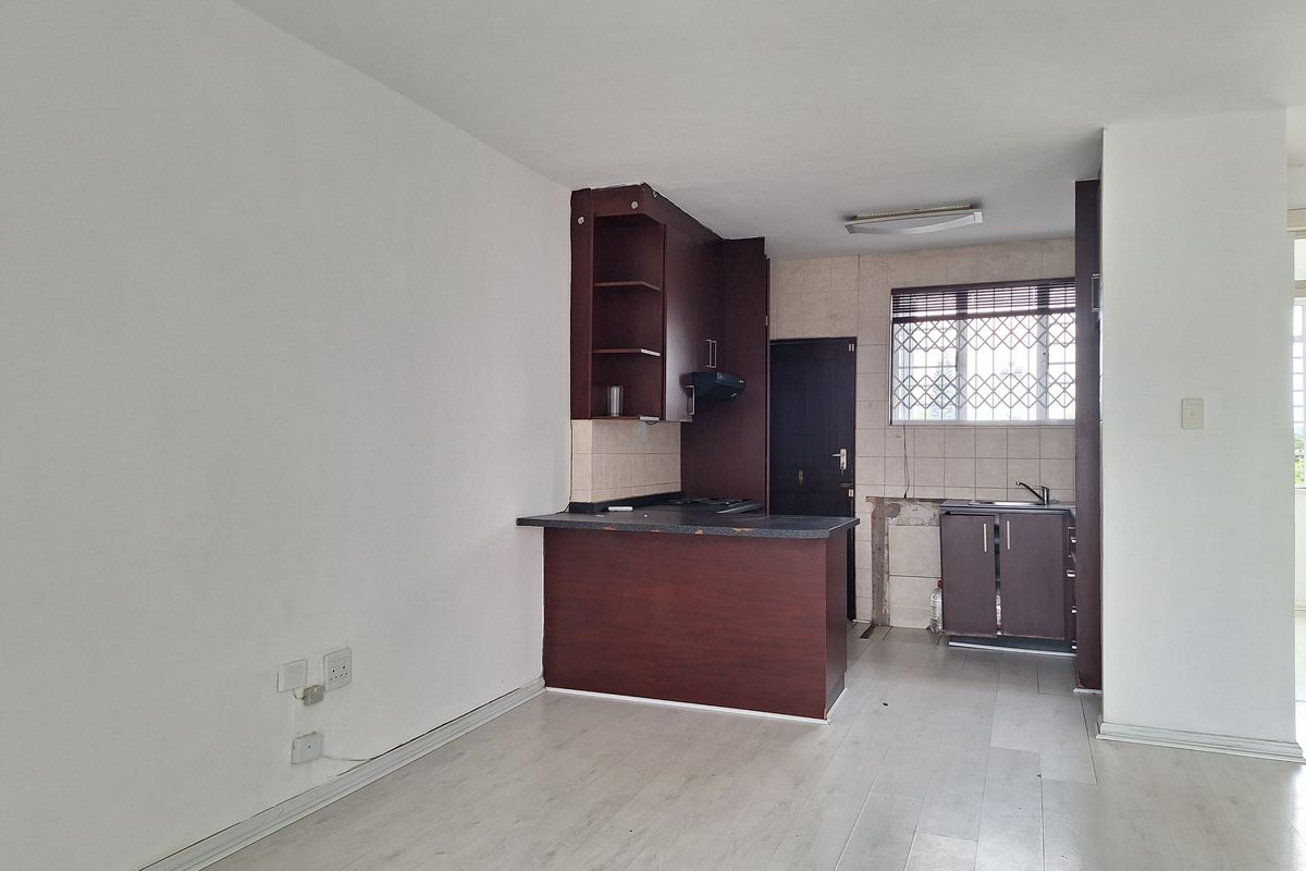 Open plan living area featuring a kitchen with dark cabinetry, breakfast bar, and laminate flooring. The space is vacant and requires minor repairs.