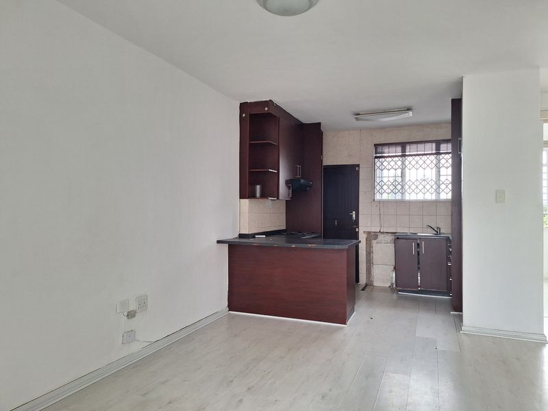 Open plan living area featuring a kitchen with dark cabinetry, breakfast bar, and laminate flooring. The space is vacant and requires minor repairs.