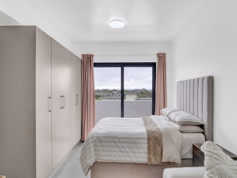 A well-maintained bedroom featuring built-in cupboards, neutral finishes, and a sliding glass door providing access to a balcony with an urban view.