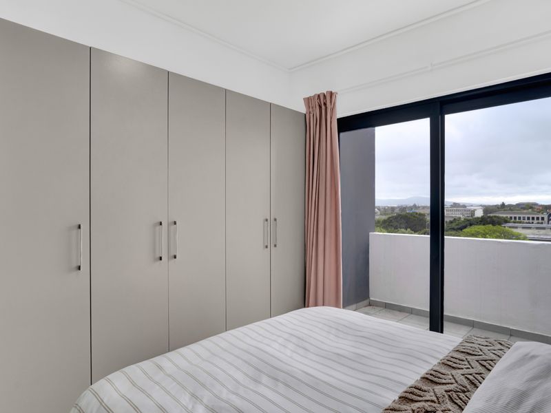 A well-maintained bedroom featuring floor-to-ceiling built-in cupboards and a sliding glass door providing direct access to a private balcony with scenic views.