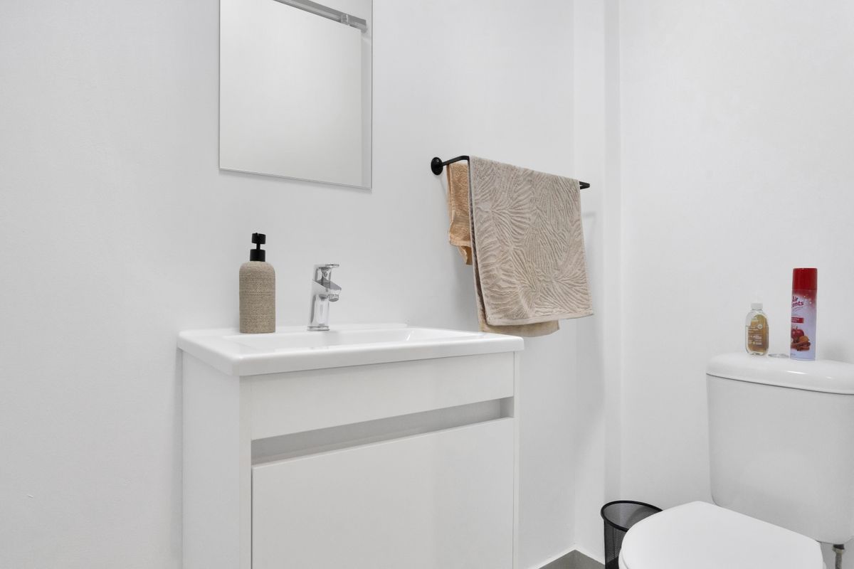 A clean and modern bathroom featuring a white vanity cabinet with a basin, a wall-mounted mirror, and a standard toilet.