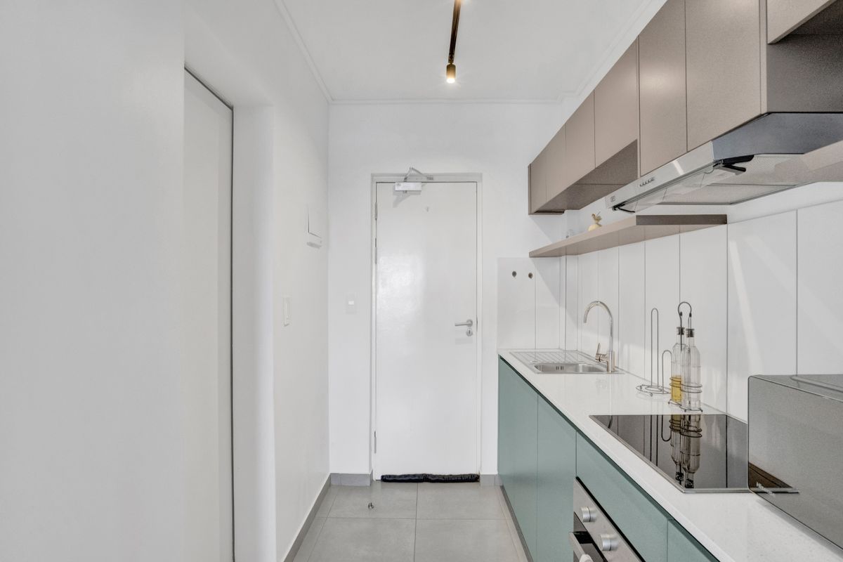 A modern, compact galley-style kitchen featuring sleek cabinetry, integrated appliances, a tiled backsplash, and durable floor tiles.
