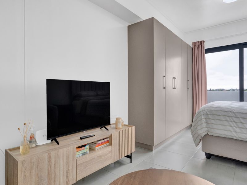 A modern bedroom featuring neutral-toned built-in wardrobes, large format floor tiles, and a sliding glass door providing access to an outdoor area.