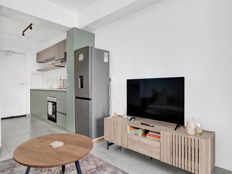 A modern open-plan living and kitchen area featuring sleek cabinetry, integrated appliances, and neutral tiled flooring, creating a functional and contemporary living space.