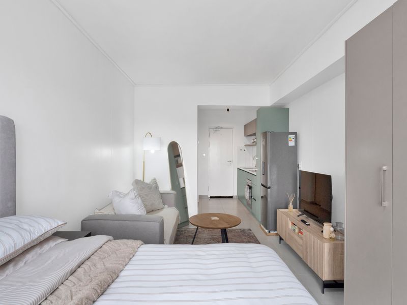 A modern open-plan studio apartment featuring a compact kitchen with built-in cabinetry, tiled floors, and a functional living and sleeping area.