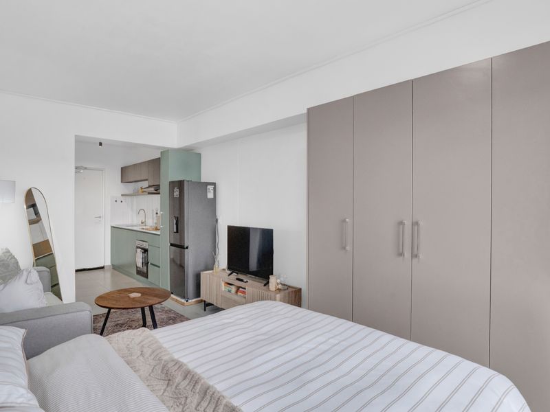 A modern open-plan studio apartment featuring a compact kitchen with built-in cabinetry and a spacious wardrobe unit.