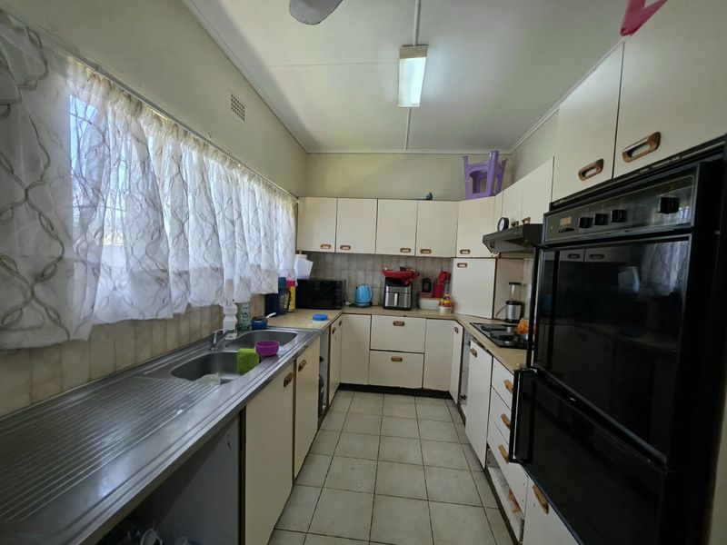 A functional kitchen featuring built-in cabinetry, a stainless steel sink, integrated oven, and cooktop, offering a dated layout ready for modernization.
