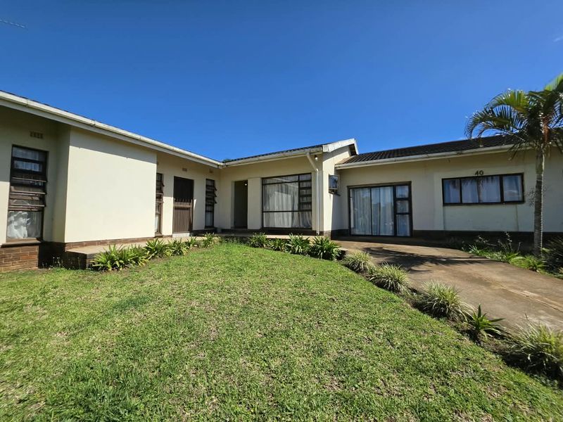 Front view of a single-story residential house featuring a concrete driveway, lawn area, and aluminium-framed windows under a clear blue sky.