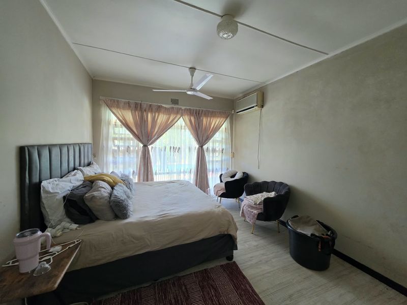 A spacious bedroom featuring a ceiling fan, split system air conditioning, and light-toned laminate flooring, offering a comfortable and functional living space.