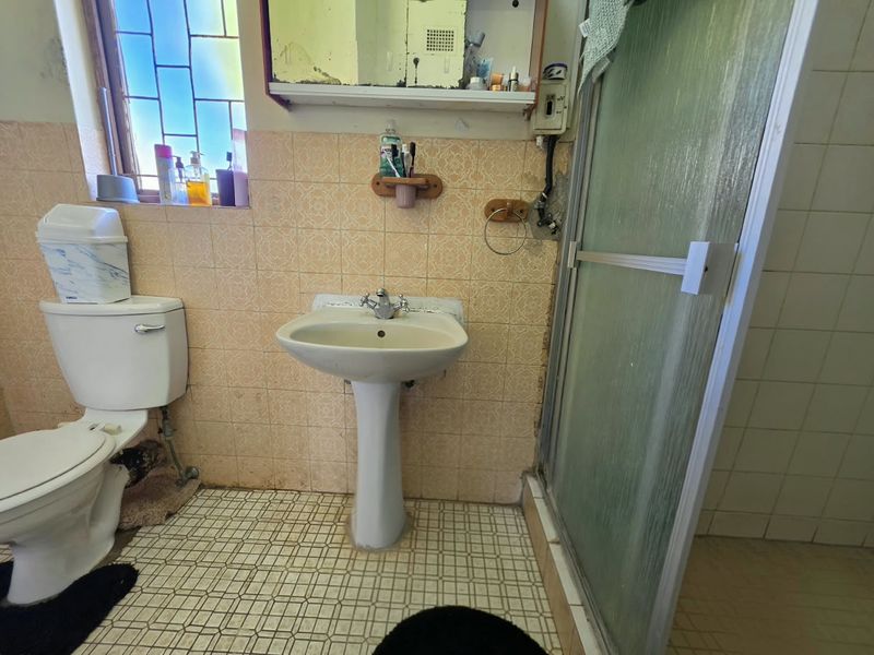 A dated bathroom featuring a pedestal basin, toilet, and shower enclosure with original wall and floor tiling, requiring modernization and cosmetic updates.