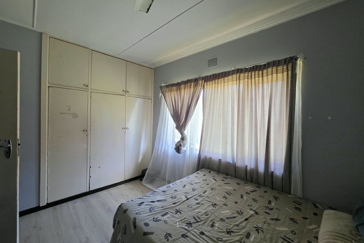 A bedroom featuring built-in cupboards, laminate flooring, and a ceiling fan, offering a functional space with potential for cosmetic updates.