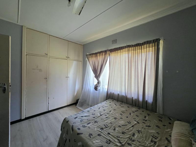 A bedroom featuring built-in cupboards, laminate flooring, and a ceiling fan, offering a functional space with potential for cosmetic updates.