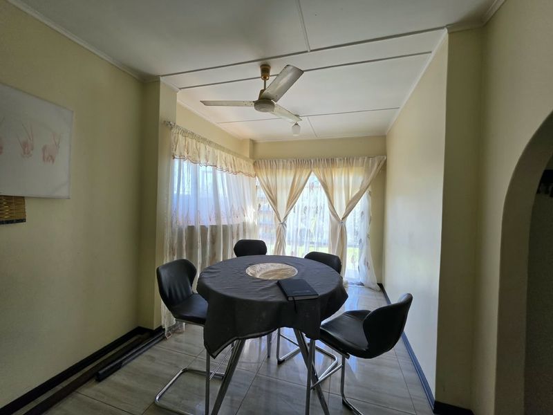 A dining area featuring tiled flooring, a ceiling fan, and large windows with curtains, offering a functional space for meals.
