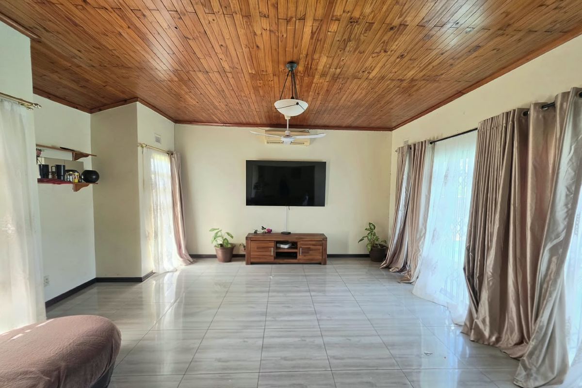 Spacious living room featuring a warm timber tongue and groove ceiling, large ceramic floor tiles, and a wall-mounted air conditioning unit.