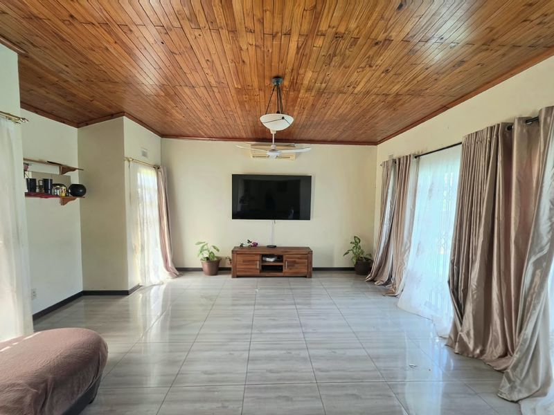 Spacious living room featuring a warm timber tongue and groove ceiling, large ceramic floor tiles, and a wall-mounted air conditioning unit.