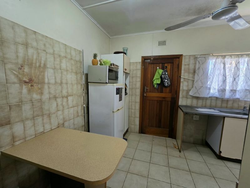 A functional kitchen featuring tiled splashbacks, built-in cabinetry, a stainless steel sink, and tiled flooring, offering potential for modernization.