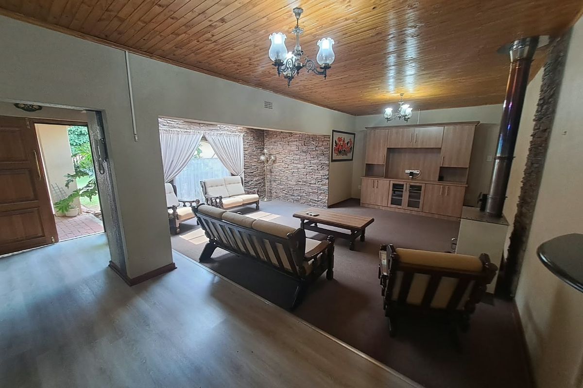 Spacious living room featuring a wood-paneled ceiling, stone accent wall, built-in cabinetry, and a freestanding fireplace, offering a warm and traditional aesthetic.