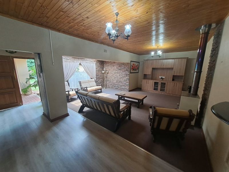 Spacious living room featuring a wood-paneled ceiling, stone accent wall, built-in cabinetry, and a freestanding fireplace, offering a warm and traditional aesthetic.